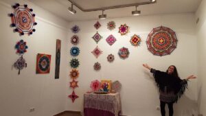 Vista de los mandalas tejidos expuestos en la Sala García-Tornel de Blanes, con una participante junto a las piezas